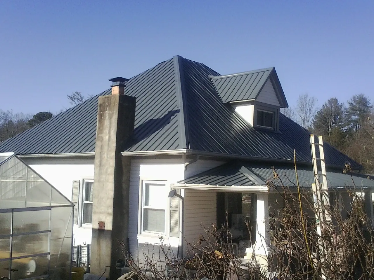 Dark blue standing seam metal roof on a white farmhouse with dormer — Slate & Tile Roof Repair by Roofing Brothers in Birch River