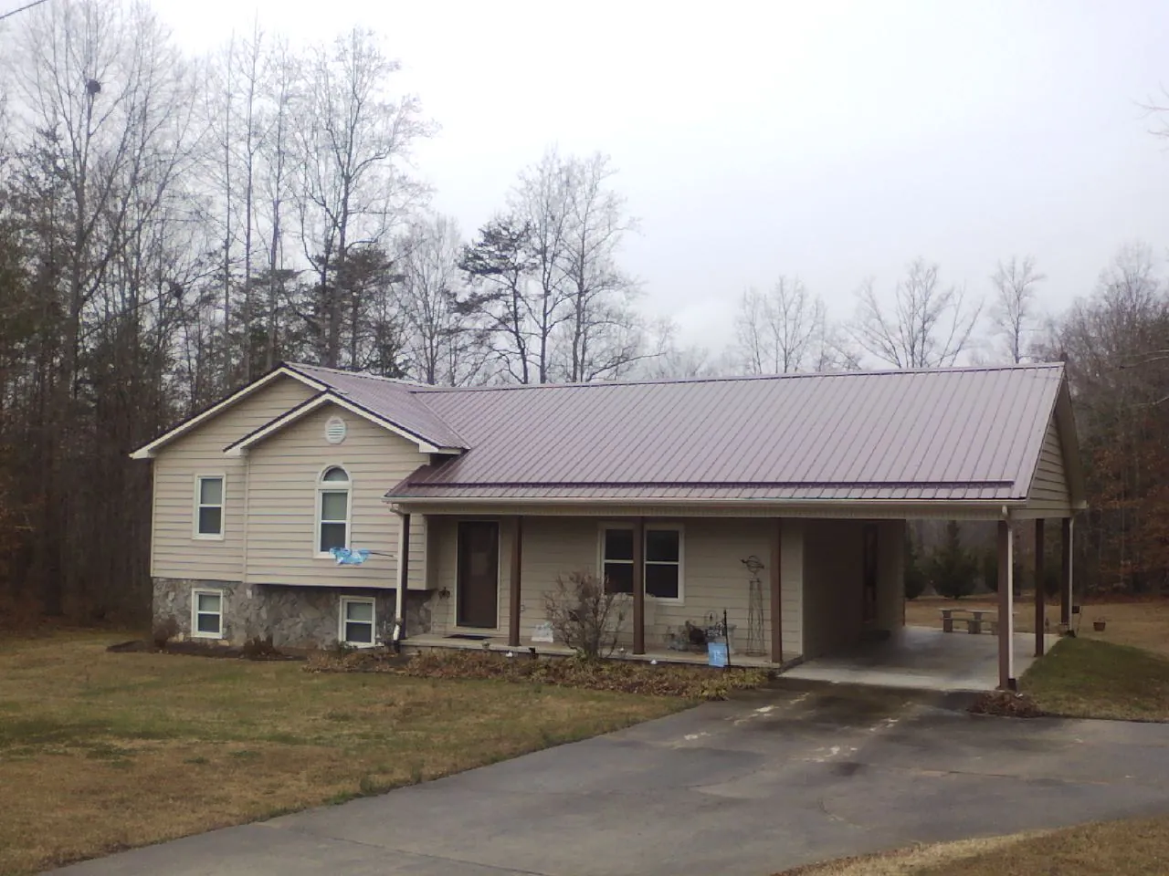 Burgundy metal roof on a tan split level home with an attached carport in Birch River