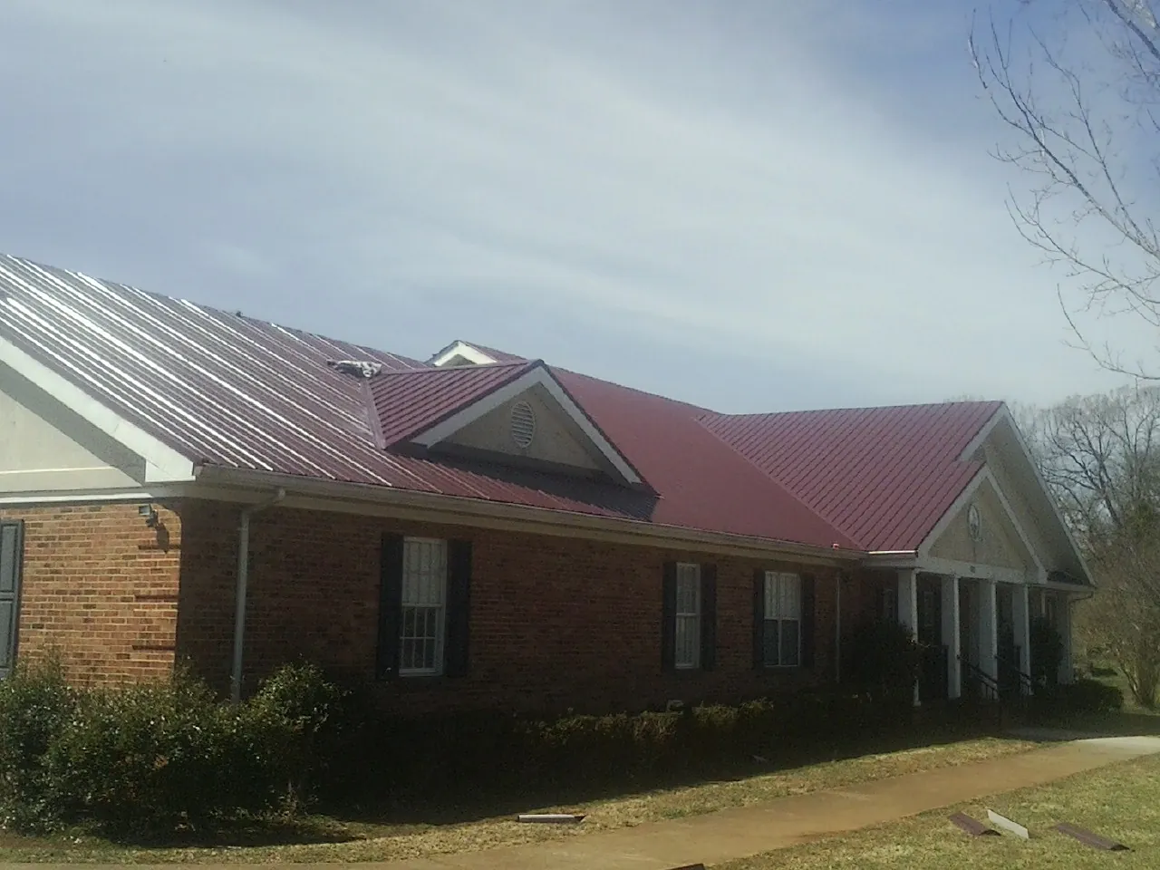 Red metal roof with gabled entries on a long brick building, from a Hail Damage Roof Repair job in Birch River