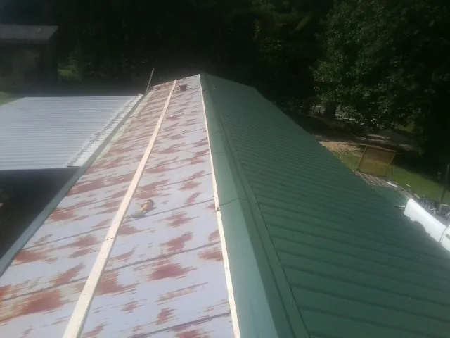 Old rusted panels beside newly installed green metal roofing — Wind Damage Roof Repair by Roofing Brothers in Birch River