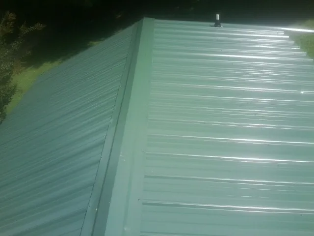 New green metal panels meeting at the ridge of a roof — Flat Roof Repair work by our crew in Birch River