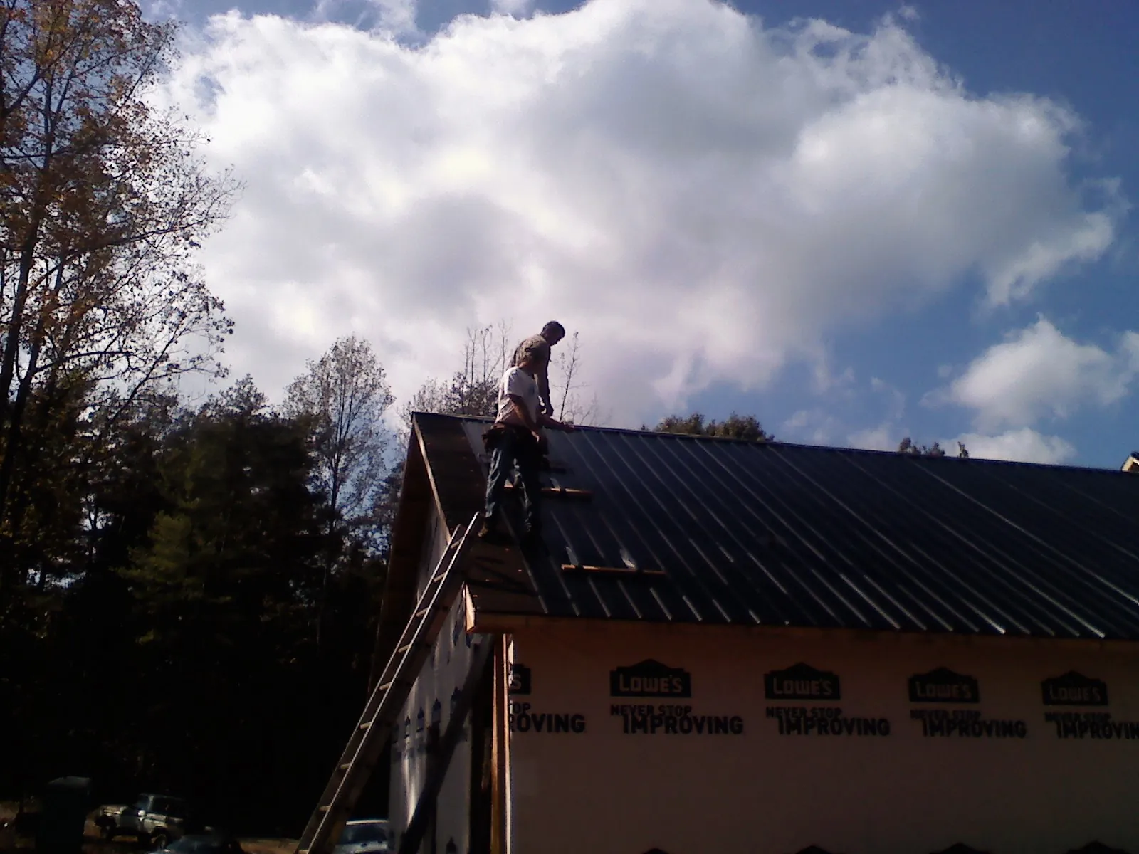 Roofer fastening dark metal panels high against a cloudy sky, from a Roof Inspection job in Birch River