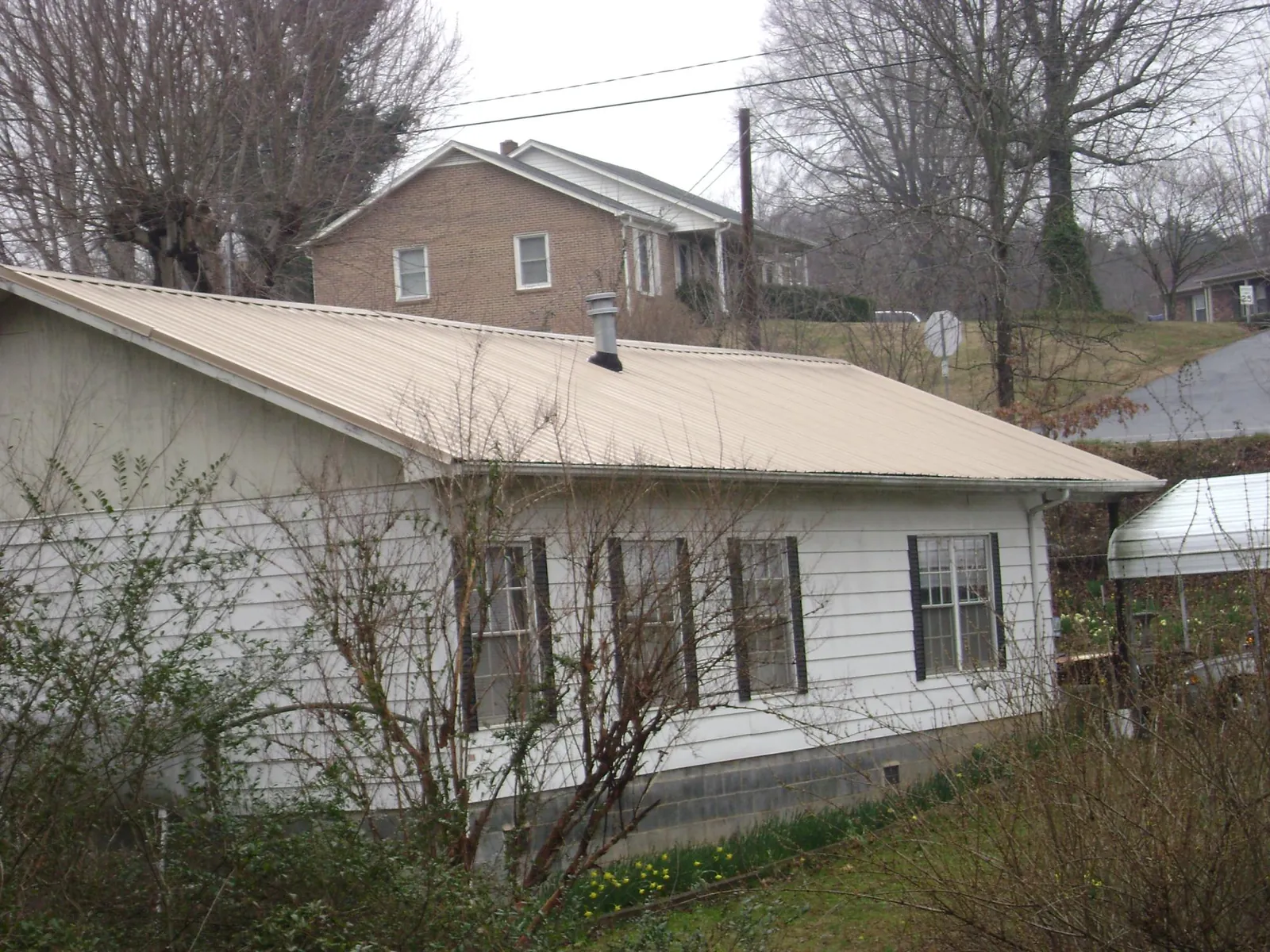 Tan metal roof on a white sided house set into a hillside — Commercial Roofing by Roofing Brothers in Birch River