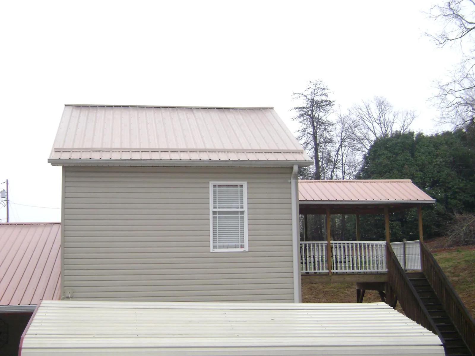 Tan metal roofs on a two story addition and attached porch, from a Roof Replacement job in Birch River